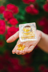 Käsi hoiab läbipaistvat klaas anumad kollaste roosiõli kapslitega